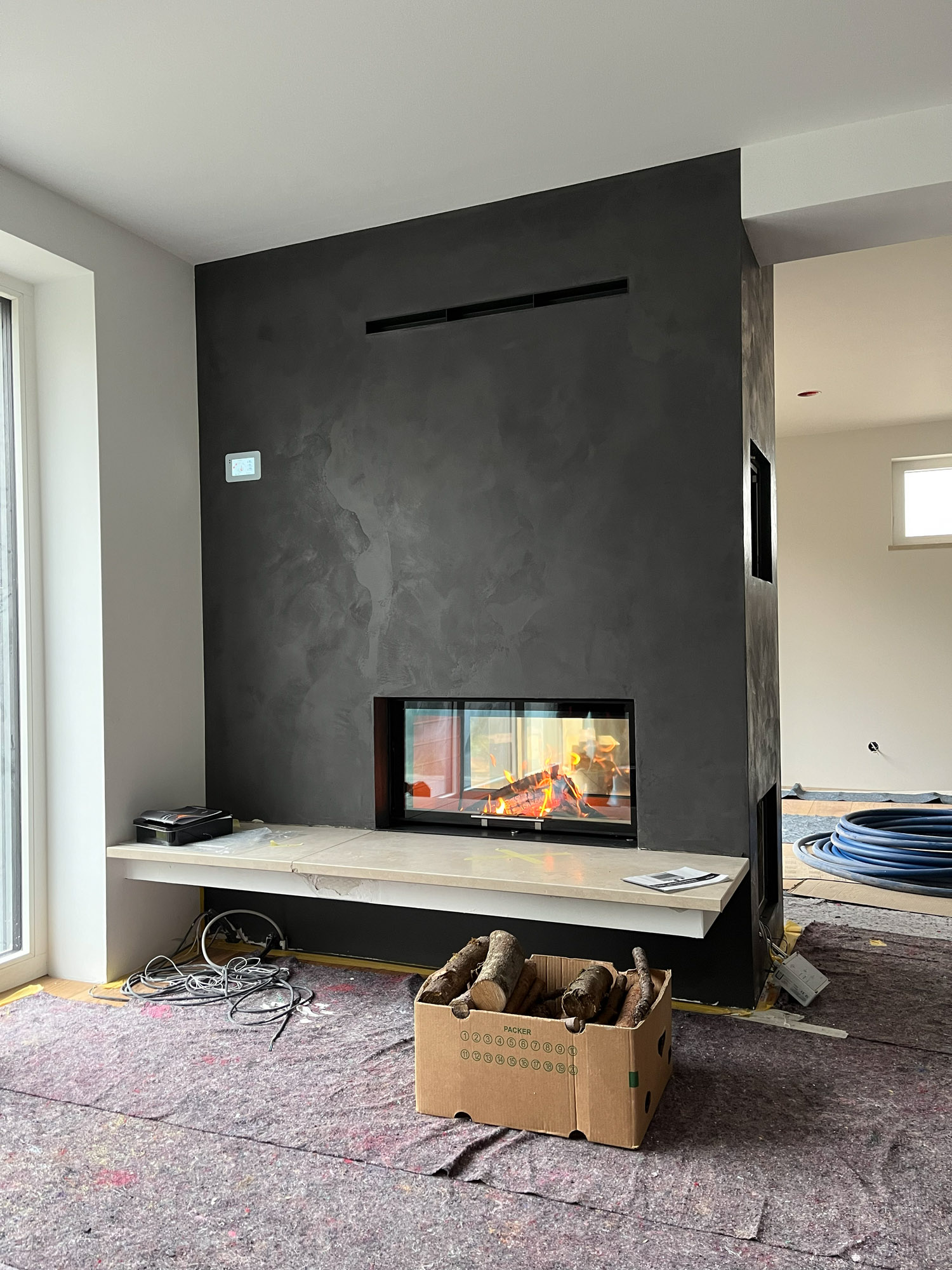 wasserführender Tunnel-Kamin als Raumteiler dunkler Kamin als Raumteiler mit einer Sitzbank davor